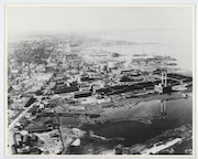 An aerial view looking southwest along the south side of Muskegon Lake at the Continental Motors Corporation Market Street Plant and Downtown Muskegon, Michigan, circa 1930s. The image is bordered by Western Avenue at bottom left corner, Lakeside area at top, and Muskegon Lake at right and bottom. Stamped on the back is 026197. ONE TIME USE ONLY